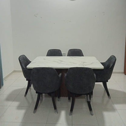 A modern dining set featuring a rectangular white marble-patterned table surrounded by six dark gray upholstered chairs, set against a plain white wall with a round wall clock.