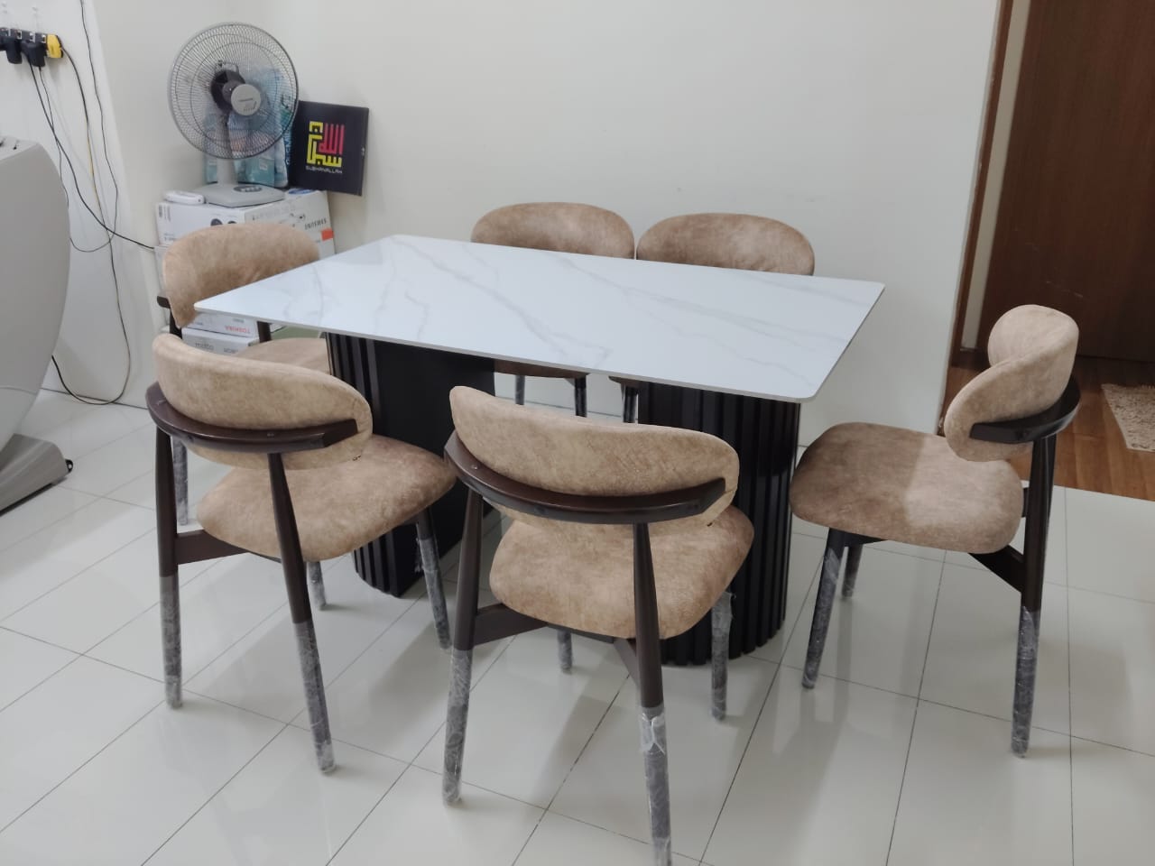 A 5-piece dining set featuring a rectangular white marble-patterned table with a black ribbed pedestal base, surrounded by four upholstered chairs in beige fabric with dark wood frames and gray metal legs.